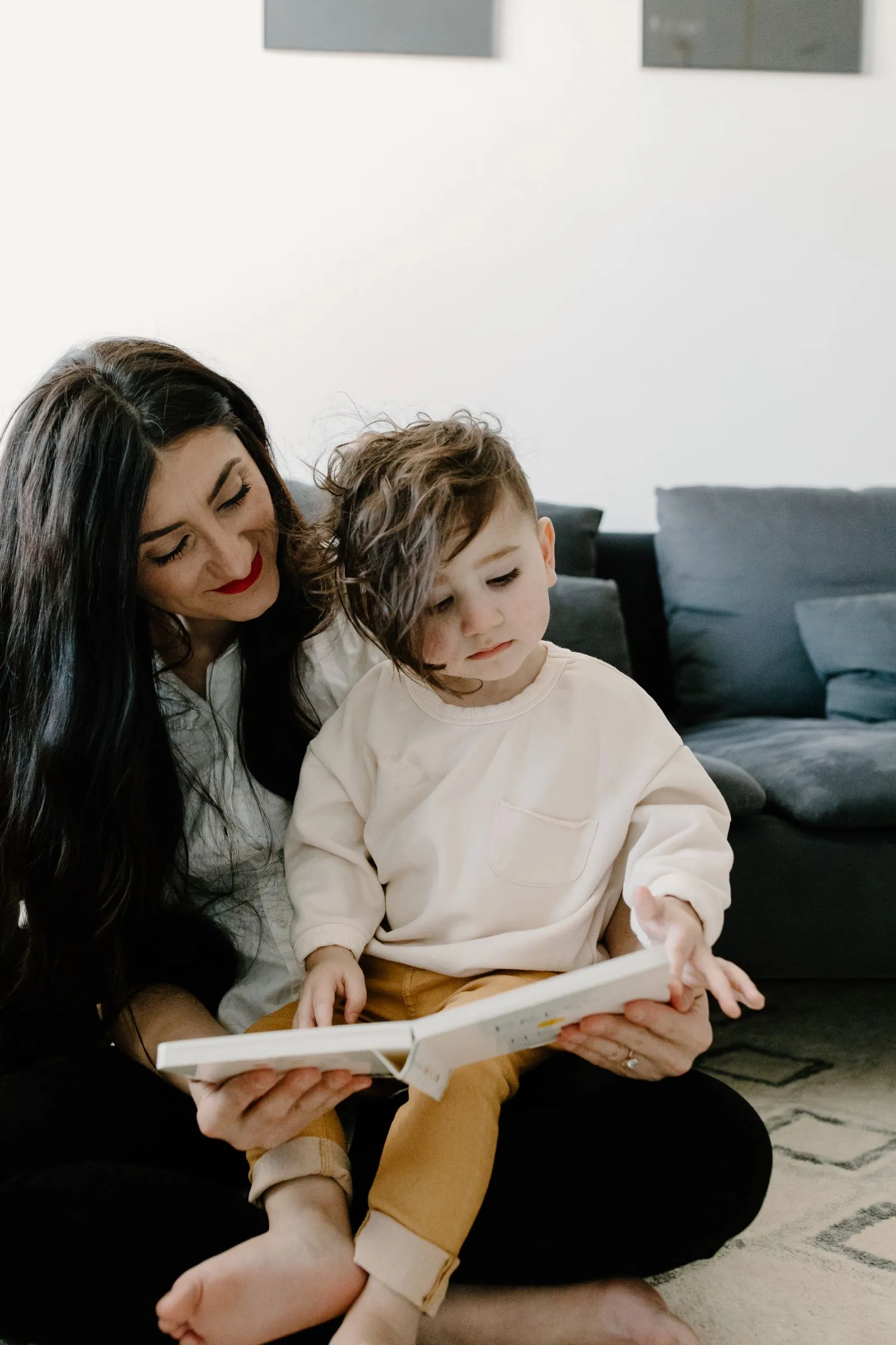 Mother and young son reading a picture book together on the living room floor